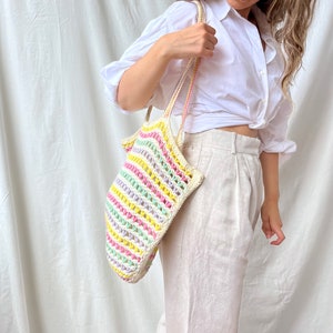 May include: A woman is holding a colorful striped crochet tote bag with a white background.