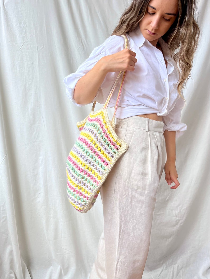 May include: A woman is holding a colorful striped crochet tote bag with a white background.