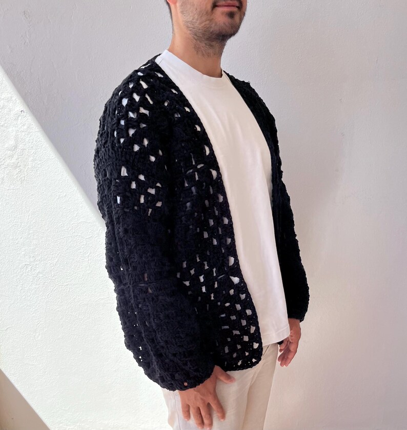 K&ouml;nnte beinhalten: Ein schwarzer H&auml;kelcardigan mit quadratischem Muster. Der Cardigan ist vorne offen und hat lange &Auml;rmel.