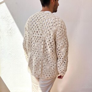 K&ouml;nnte beinhalten: Ein geh&auml;kelter Cardigan in Cremefarbe mit einem quadratischen Muster. Der Cardigan hat lange &Auml;rmel und einen V-Ausschnitt.