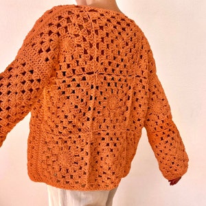May include: A crocheted sweater in a burnt orange color. The sweater has a loose fit and a square pattern.