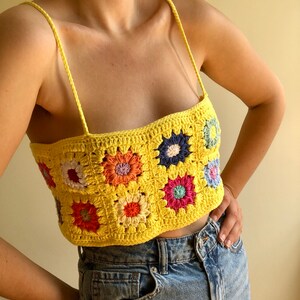 May include: A yellow crochet top with a colorful floral pattern. The top is sleeveless and has a square neckline.