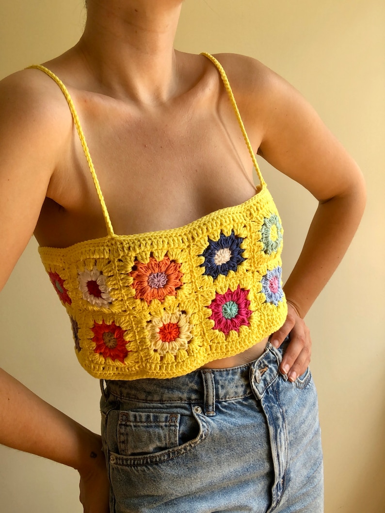 May include: A yellow crochet top with a colorful floral pattern. The top is sleeveless and has a square neckline.