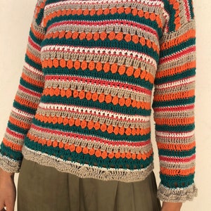May include: A striped crochet sweater with a loose fit and long sleeves. The sweater is made with a variety of colors, including orange, green, beige, and pink. The sweater has a textured design with small, raised dots.