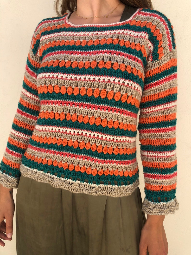 May include: A striped crochet sweater with a loose fit and long sleeves. The sweater is made with a variety of colors, including orange, green, beige, and pink. The sweater has a textured design with small, raised dots.