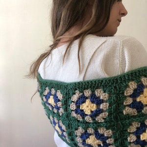 May include: A green, blue, and beige crocheted granny square shawl. The shawl is made with a variety of different colored yarn and has a unique, handmade look.