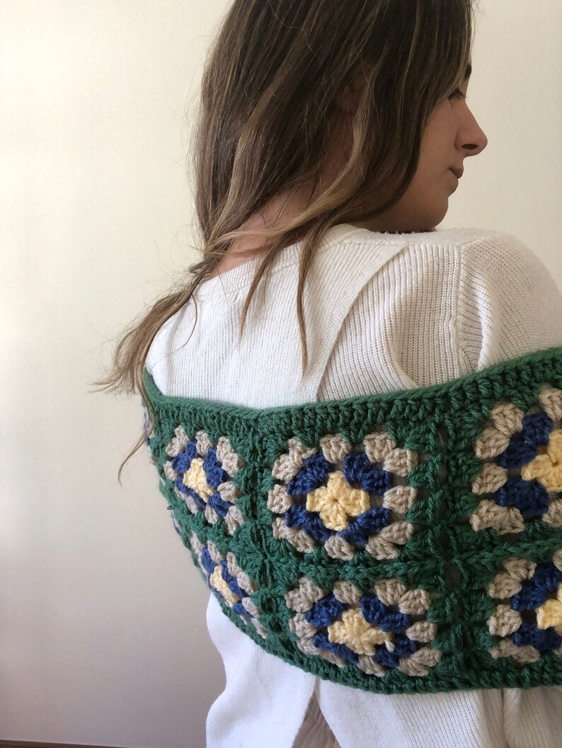May include: A green, blue, and beige crocheted granny square shawl. The shawl is made with a variety of different colored yarn and has a unique, handmade look.