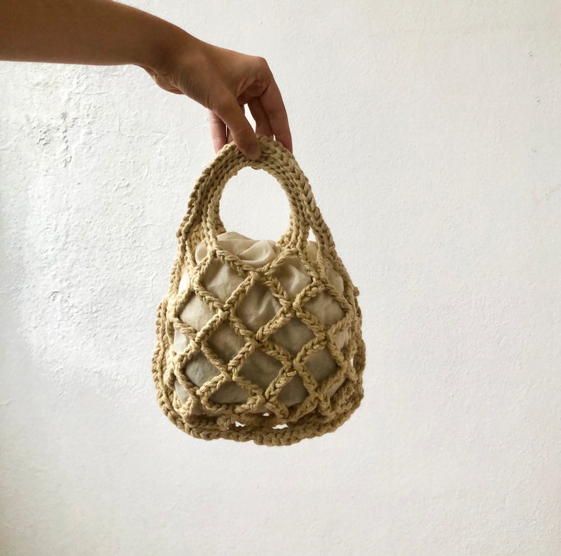 May include: A beige crocheted mesh bag with a fabric lining. The bag has a single handle and is designed for carrying small items.