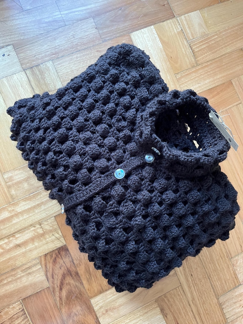 May include: A black crocheted cardigan with a button closure. The cardigan has a textured, puffy design.