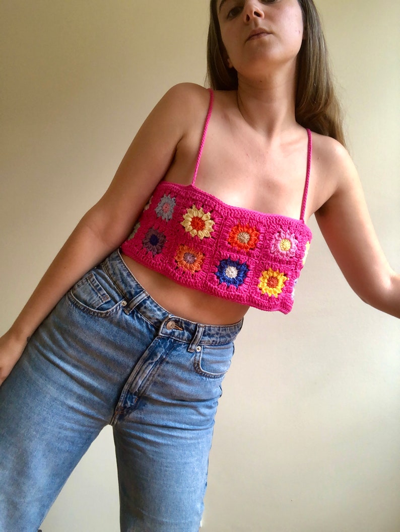 May include: A pink crochet top with colorful flower designs. The top is sleeveless and has a square neckline.