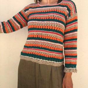 May include: A striped crochet sweater with a textured design in shades of orange, green, beige, and white. The sweater has long sleeves and a scoop neck.