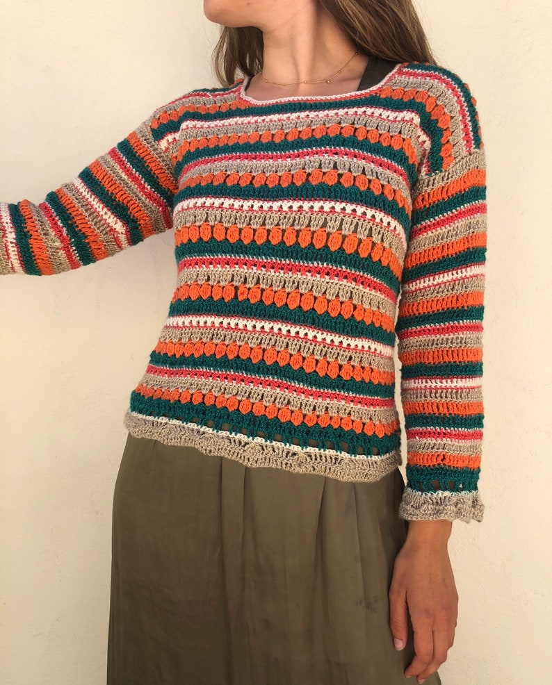 May include: A striped crochet sweater with a textured design in shades of orange, green, beige, and white. The sweater has long sleeves and a scoop neck.