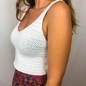 May include: White crochet tank top with a v-neckline. The top is made of a lightweight, breathable fabric and has a relaxed fit.