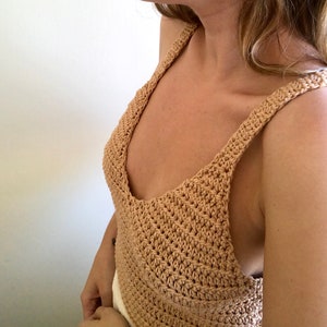 May include: A crocheted tank top with a wide, V-shaped neckline and thin straps. The top is made of a light brown yarn.
