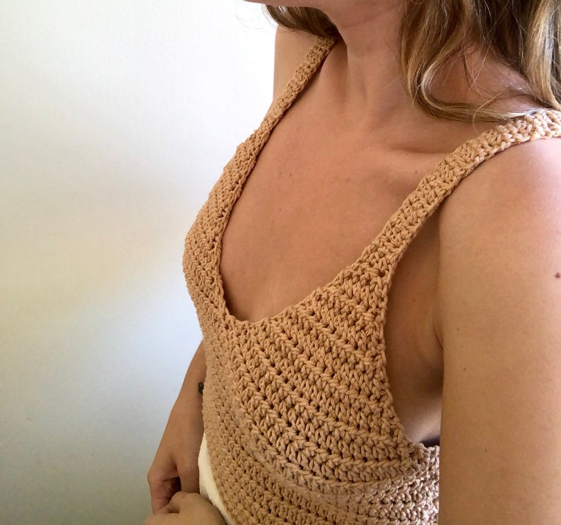 May include: A crocheted tank top with a wide, V-shaped neckline and thin straps. The top is made of a light brown yarn.