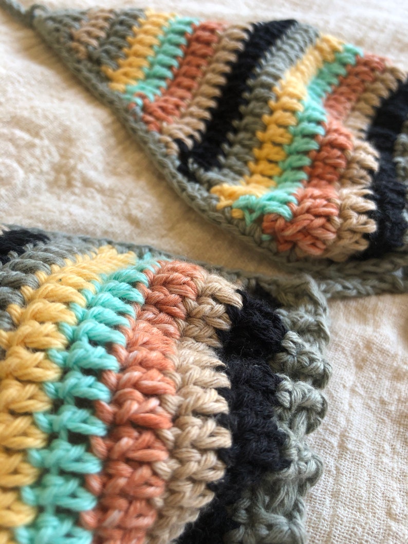 Op de afbeelding: Close-up van een gehaakt topje met een gestreept patroon in tinten groen, zwart, beige, geel en lichtblauw.