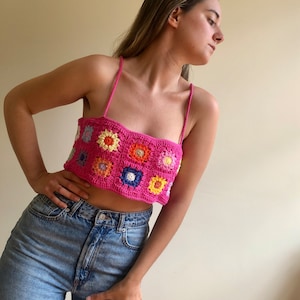 K&ouml;nnte beinhalten: Ein leuchtend pinkfarbenes H&auml;keltop mit floralem Muster. Das Top hat ein quadratisches Design mit bunten Blumenmotiven in Orange, Gelb, Blau und Wei&szlig;. Es hat d&uuml;nne Spaghettitr&auml;ger.