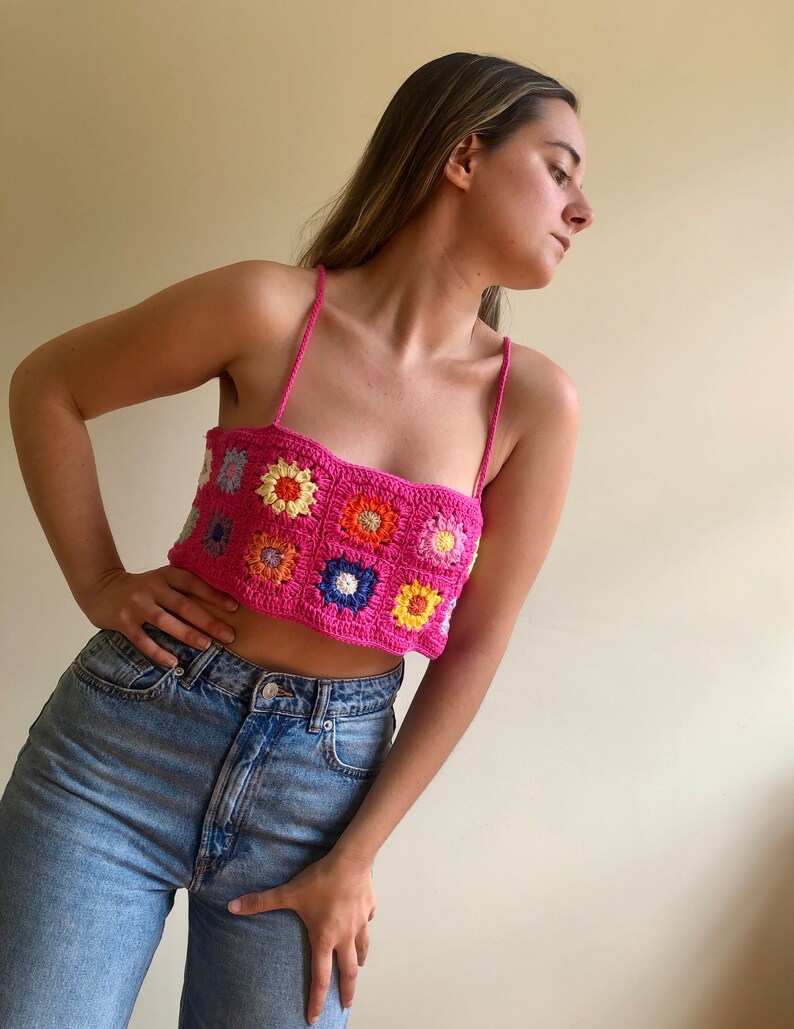 K&ouml;nnte beinhalten: Ein leuchtend pinkfarbenes H&auml;keltop mit floralem Muster. Das Top hat ein quadratisches Design mit bunten Blumenmotiven in Orange, Gelb, Blau und Wei&szlig;. Es hat d&uuml;nne Spaghettitr&auml;ger.