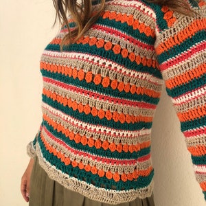 May include: A striped crochet top with long sleeves in shades of orange, green, beige, and pink. The top has a loose fit and a relaxed style.