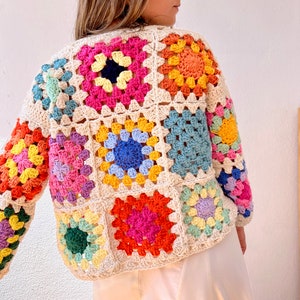 May include: A colorful crochet cardigan with a granny square pattern in shades of pink, blue, yellow, green, and orange. The cardigan is made with a cream-colored yarn.