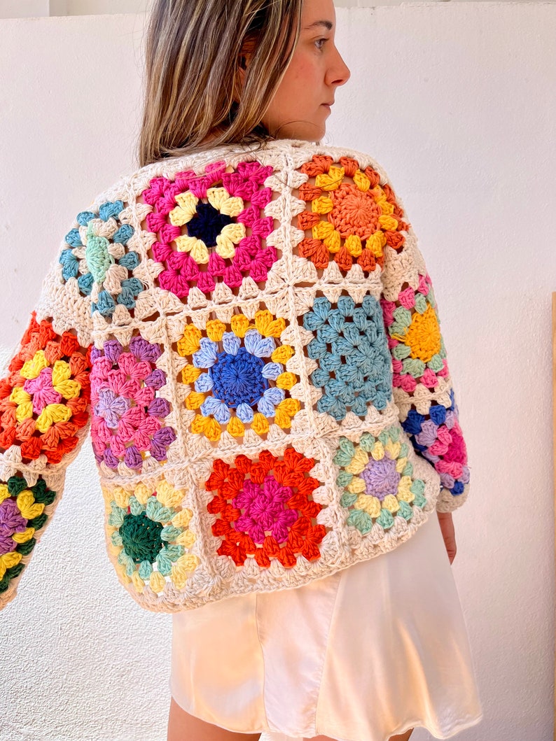 May include: A colorful crochet cardigan with a granny square pattern in shades of pink, blue, yellow, green, and orange. The cardigan is made with a cream-colored yarn.