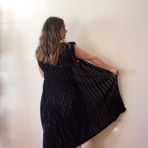Puede incluir: Un chaleco de crochet negro con un frente largo y abierto y sin mangas.