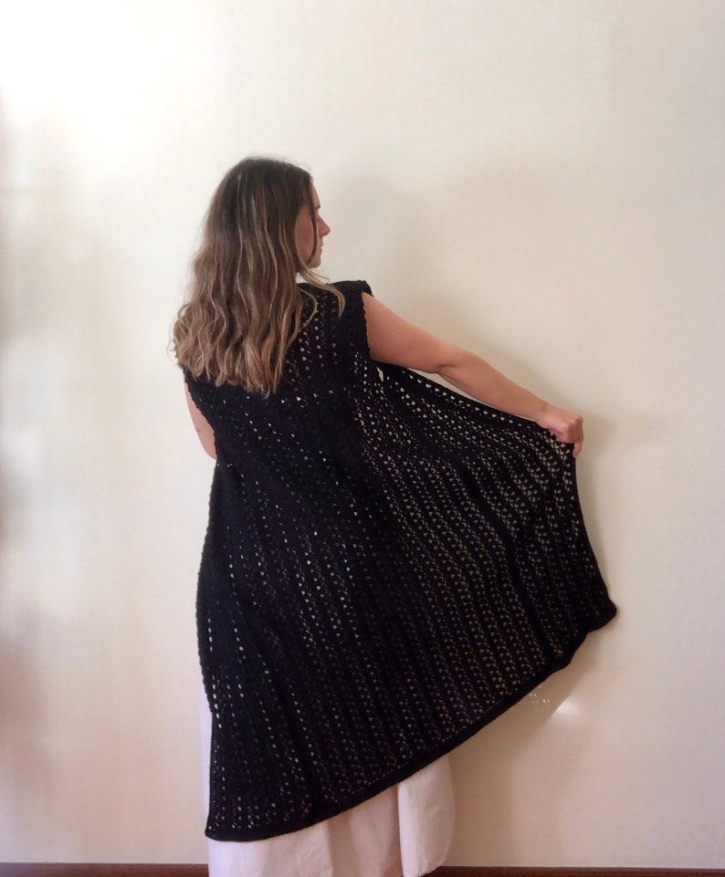 Puede incluir: Un chaleco de crochet negro con un frente largo y abierto y sin mangas.