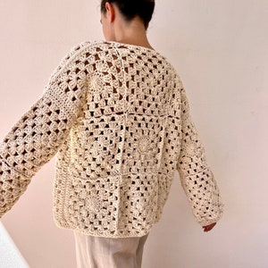 May include: A cream-colored crocheted cardigan with a square pattern. The cardigan has long sleeves and a relaxed fit.