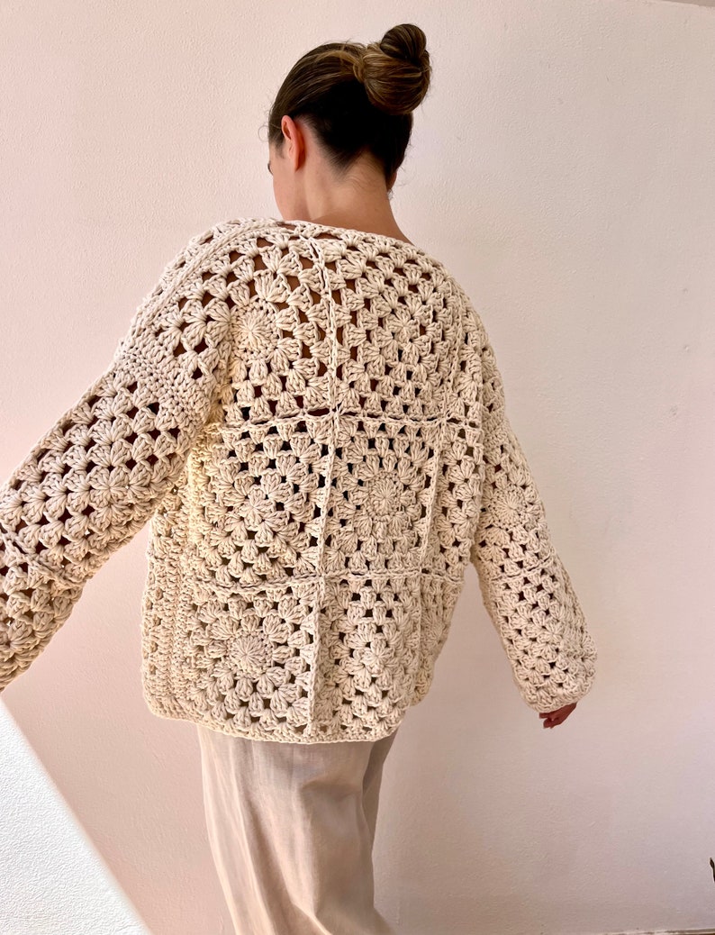 May include: A cream-colored crocheted cardigan with a square pattern. The cardigan has long sleeves and a relaxed fit.
