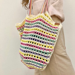May include: A colorful crocheted tote bag with a striped pattern in pink, yellow, green, and purple. The bag is made of a lightweight, breathable material and has a wide, comfortable handle.