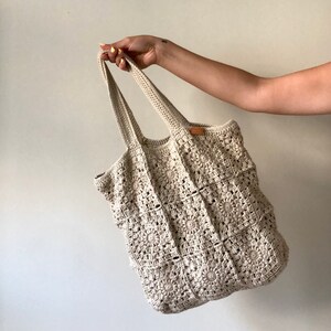 May include: A crocheted tote bag with a square pattern in a cream color. The bag has two long straps.