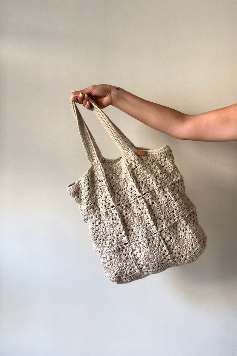 May include: A crocheted tote bag with a square pattern in a cream color. The bag has two long straps.
