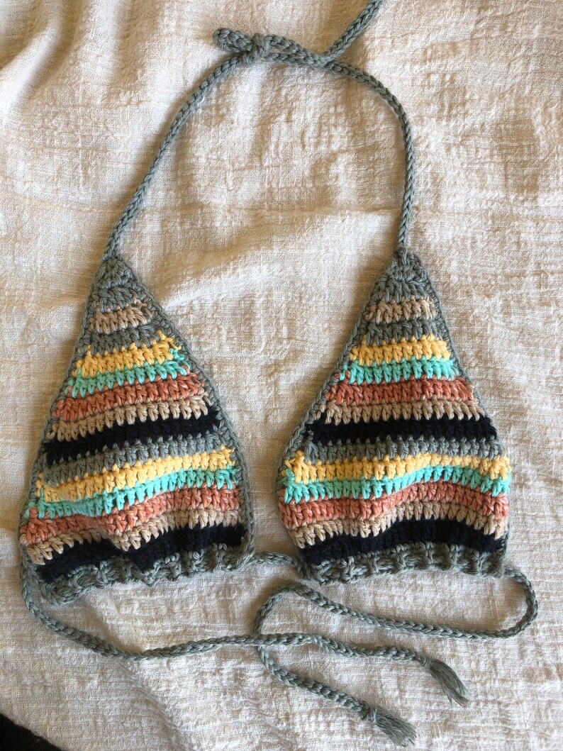 Op de afbeelding: Een gehaakt bikini-topje met een gestreept patroon in tinten zwart, grijs, geel, roze en blauw. Het topje heeft verstelbare bandjes en strikjes aan de achterkant.