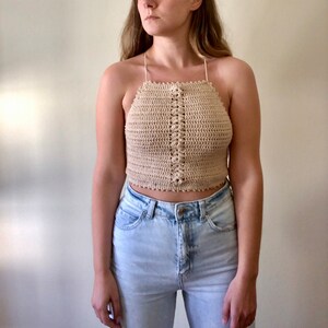 May include: A beige crochet halter top with a button closure at the front. The top is cropped and has a scalloped edge.