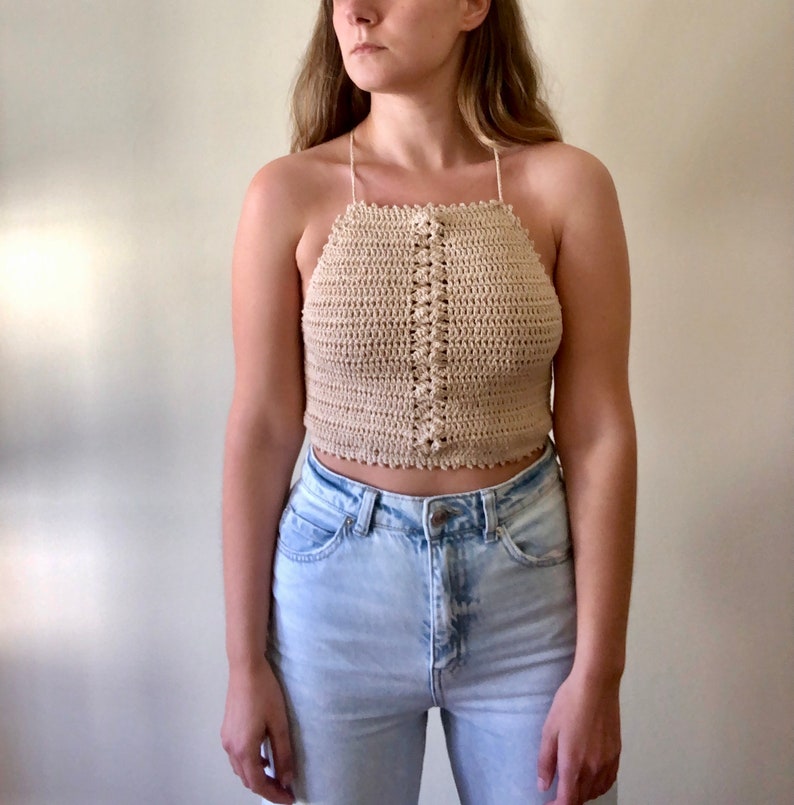 May include: A beige crochet halter top with a button closure at the front. The top is cropped and has a scalloped edge.
