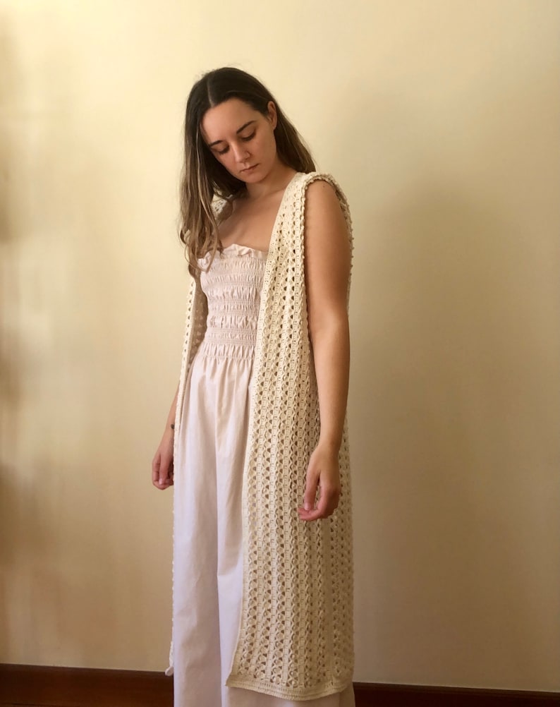 Puede incluir: Un chaleco largo de crochet de color crema, de corte holgado y abierto por delante. El chaleco est&aacute; hecho con un delicado patr&oacute;n de punto calado.