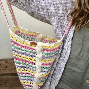 May include: A white crochet tote bag with pink, yellow, and green stripes. The bag has a brown leather tag with the word "Handmade" on it.
