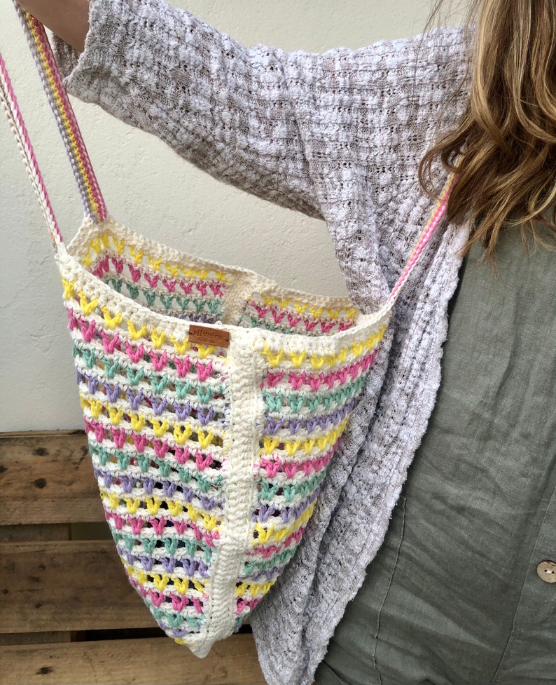 May include: A white crochet tote bag with pink, yellow, and green stripes. The bag has a brown leather tag with the word "Handmade" on it.