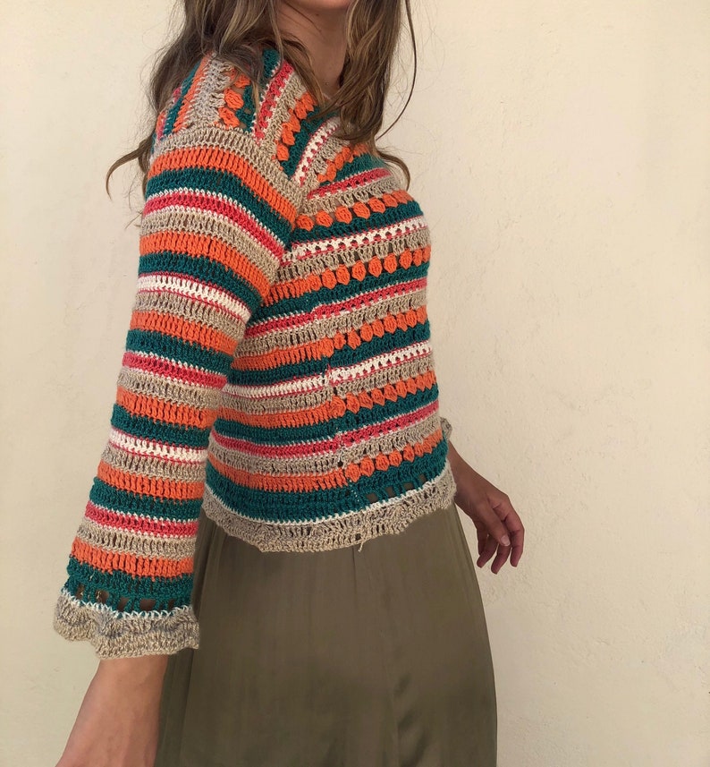 May include: A striped crochet top with a bell sleeve. The top is made with a combination of beige, orange, green, and pink yarn.