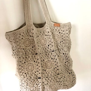 May include: A beige crocheted tote bag with a brown leather tag. The bag is made of a square pattern with a circular design in the center of each square.