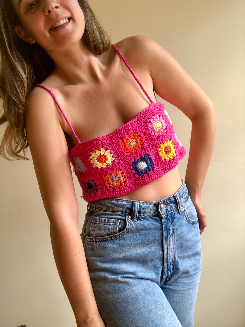 May include: A pink crochet top with colorful flower designs. The top has thin straps and a square neckline.