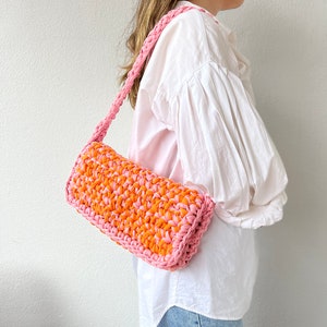 May include: A pink and orange crocheted shoulder bag with a long strap.