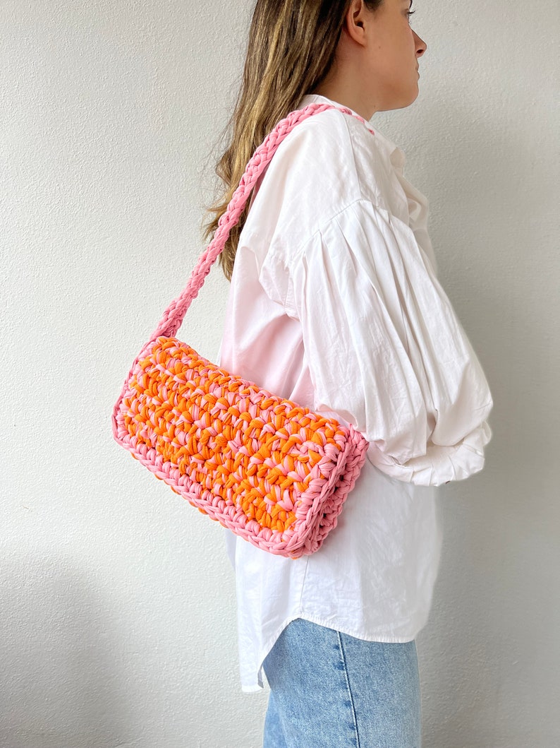 May include: A pink and orange crocheted shoulder bag with a long strap.