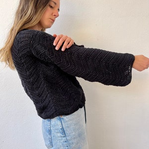 May include: A black crocheted sweater with a loose fit and long sleeves. The sweater has a textured pattern and is worn with light blue jeans.