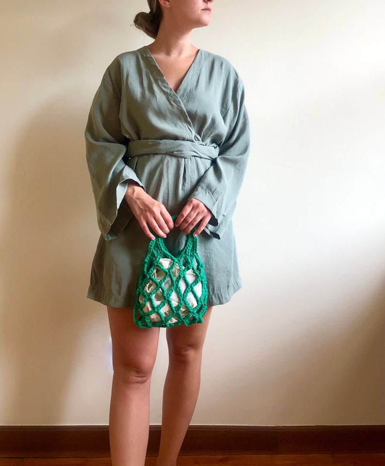 May include: A woman wearing a sage green wrap dress with long sleeves and a green crocheted mesh bag.