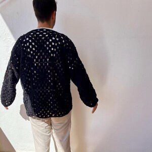 K&ouml;nnte beinhalten: Ein schwarzer H&auml;kelpullover mit quadratischem Muster. Der Pullover hat lange &Auml;rmel und eine lockere Passform.