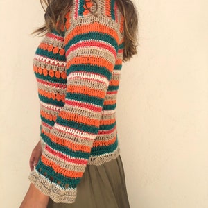 May include: A striped crochet top with orange, green, beige, and pink stripes. The top has a loose fit and a slightly cropped length.