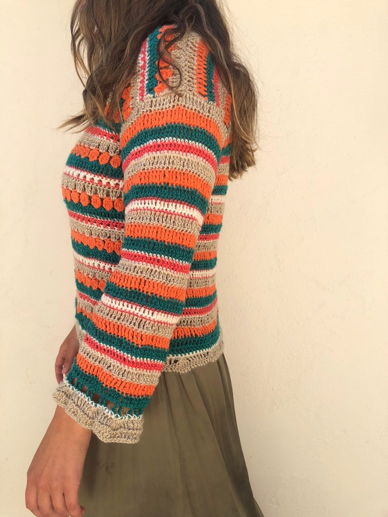 May include: A striped crochet top with orange, green, beige, and pink stripes. The top has a loose fit and a slightly cropped length.