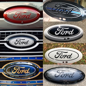 May include: A collection of Ford emblem replacements in various colors and designs. The emblems feature the Ford logo in different styles, including red, black, white, and a design with the American flag.