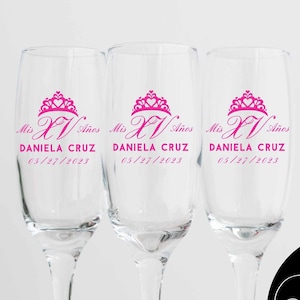 May include: Three clear glass champagne flutes with pink lettering that reads "Mis XV Anos" and "DANIELA CRUZ 05/27/2023".